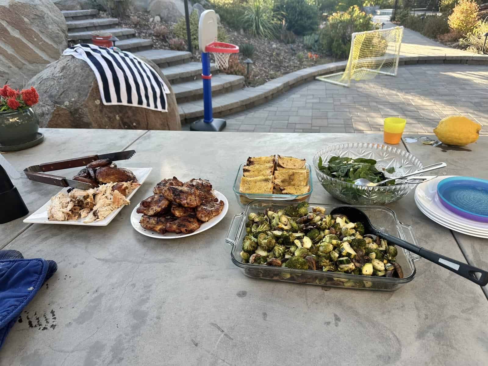 An outdoor BBQ dinner spread with grilled meats and sides