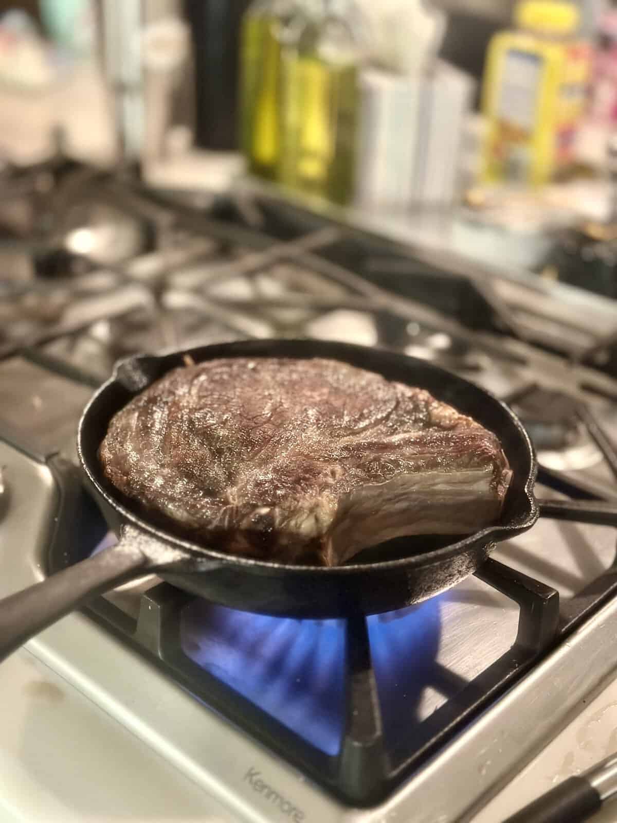 Ribeye steak searing in a hot cast-iron skillet with flames